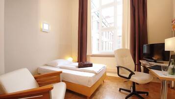 A hotel room with a bed, a desk with a computer, a chair, and a window with curtains.