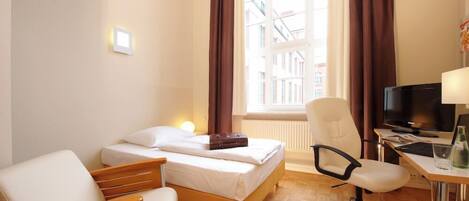 A hotel room with a bed, a desk with a computer, a chair, and a window with curtains.
