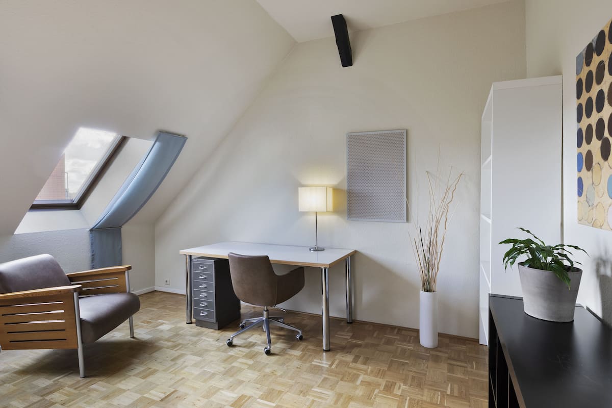 Ein modernes Schlafzimmer im Loft-Stil mit Schräge, Dachfenster, Schreibtisch mit Stuhl, Nachttisch und einer Topfpflanze.