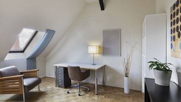 Un dormitorio estilo loft moderno con techo inclinado, tragaluces, un escritorio con silla, una mesita de noche y una planta en maceta.