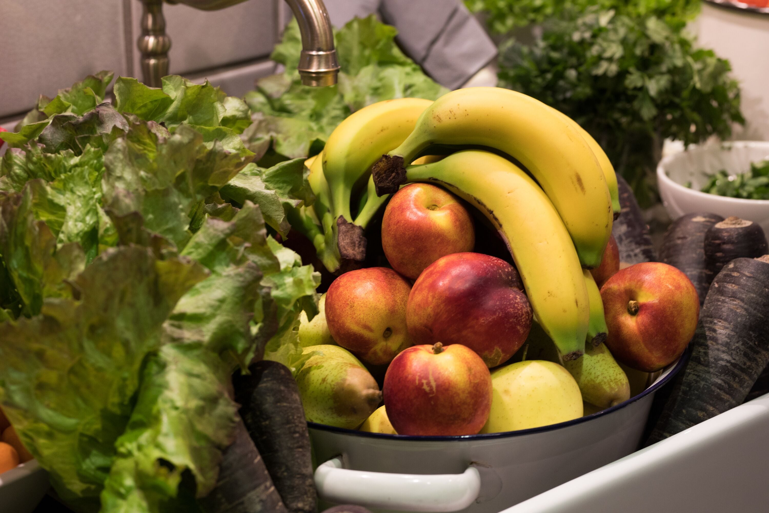 A kitchen sink with fresh fruits and vegetables, including apples, bananas, and lettuce.