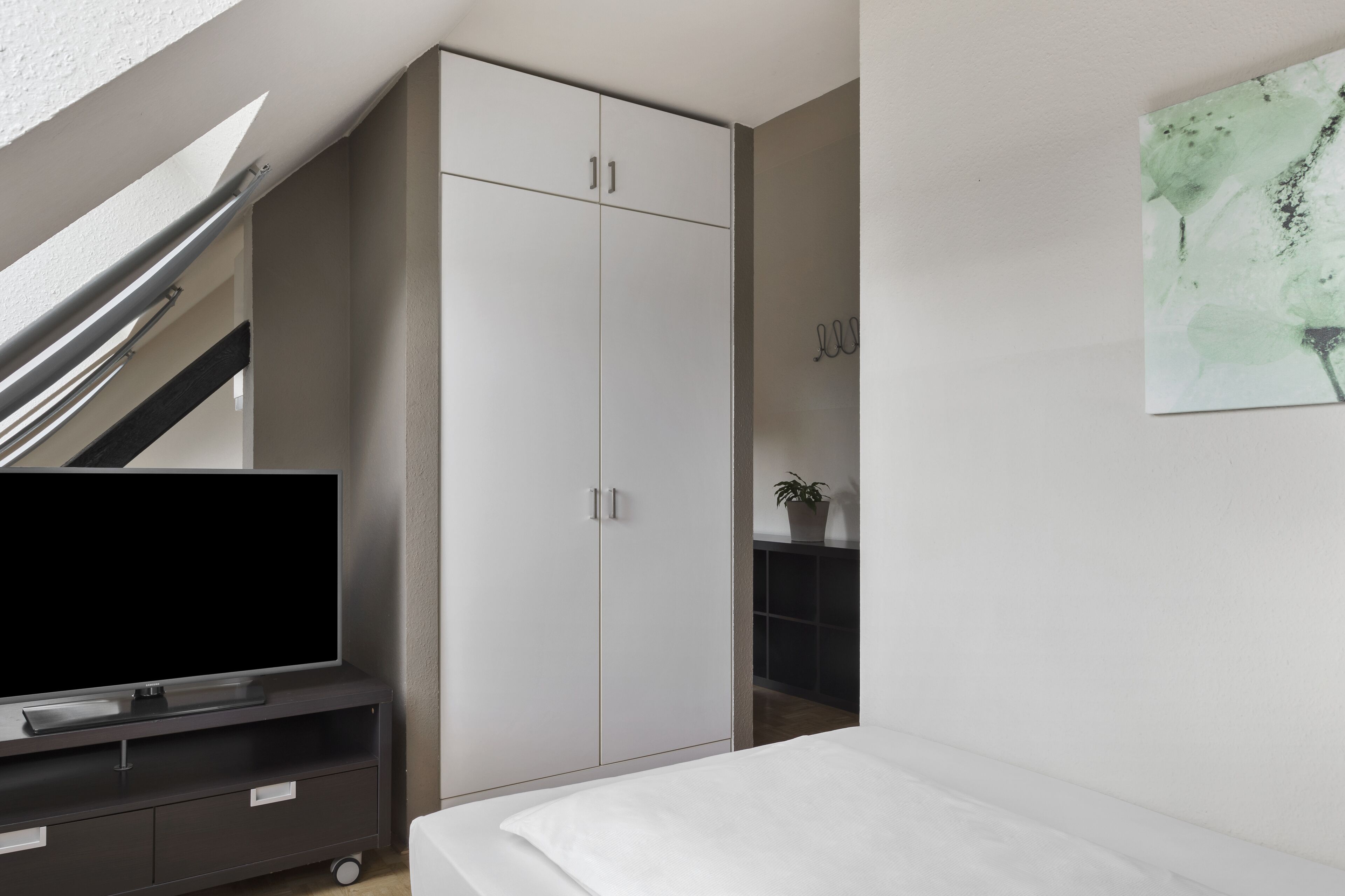 A bedroom with a bed, a TV on a stand, a wardrobe, and a staircase.