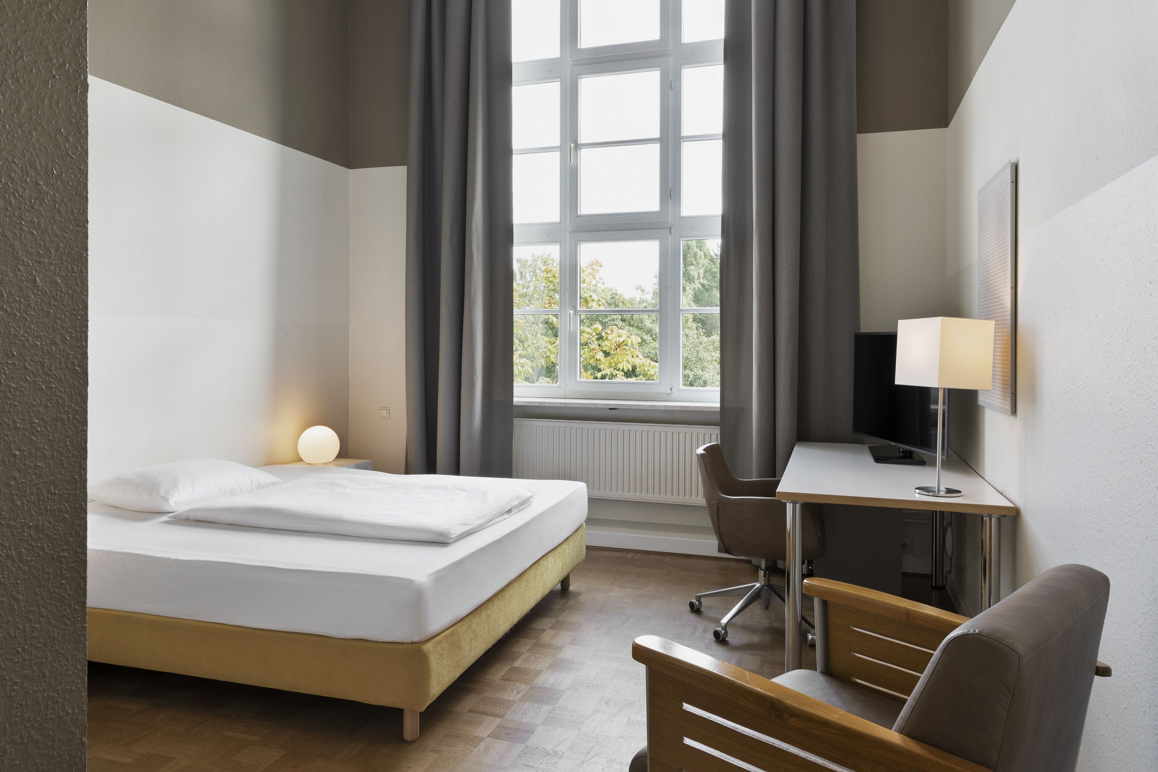 A hotel room with a bed, desk, chair, and a window with curtains.