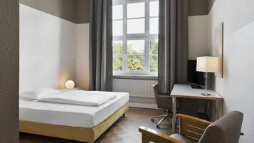 A hotel room with a bed, desk, chair, and a window with curtains.