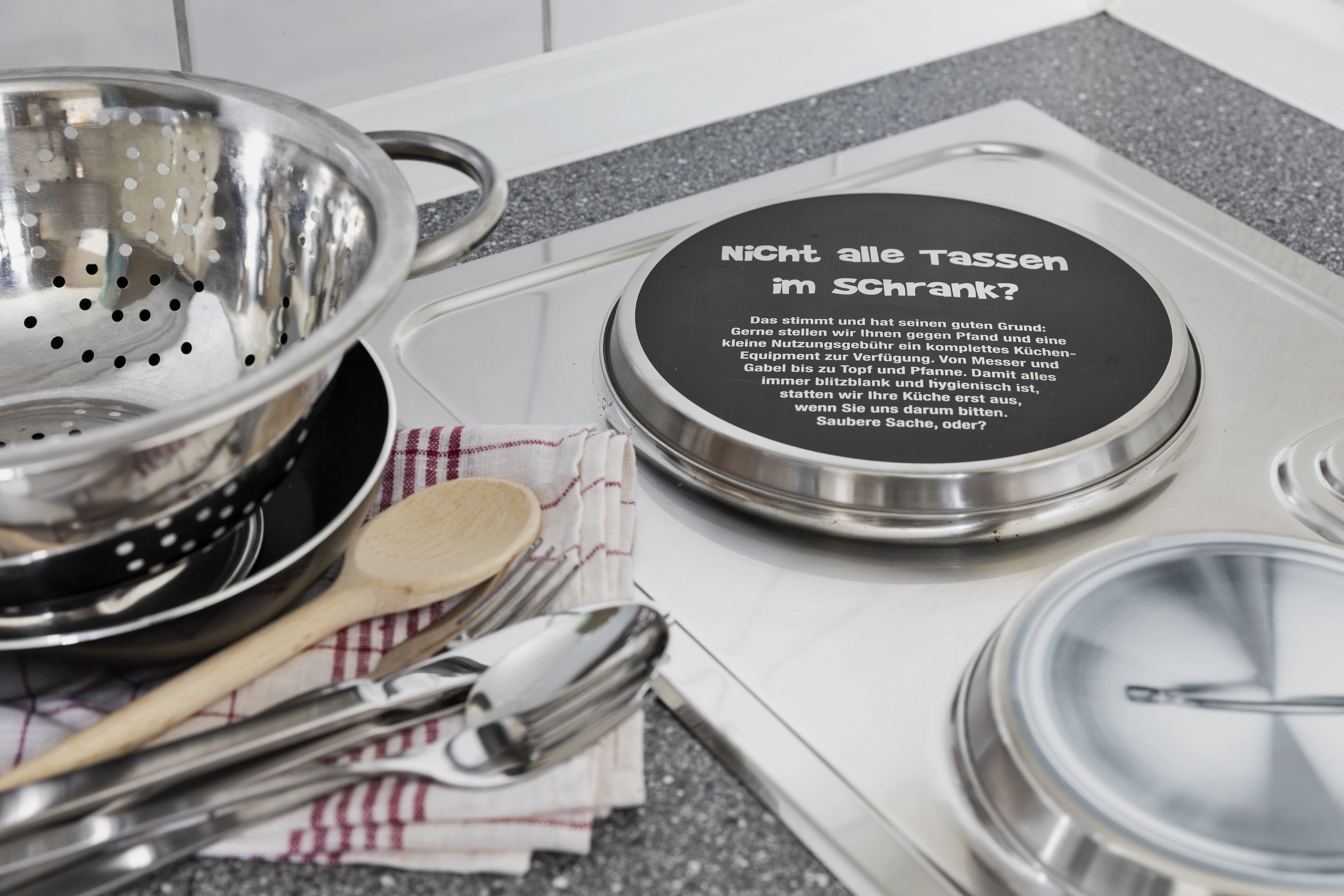 A kitchen sink with a stainless steel colander and a dish with a message in German.