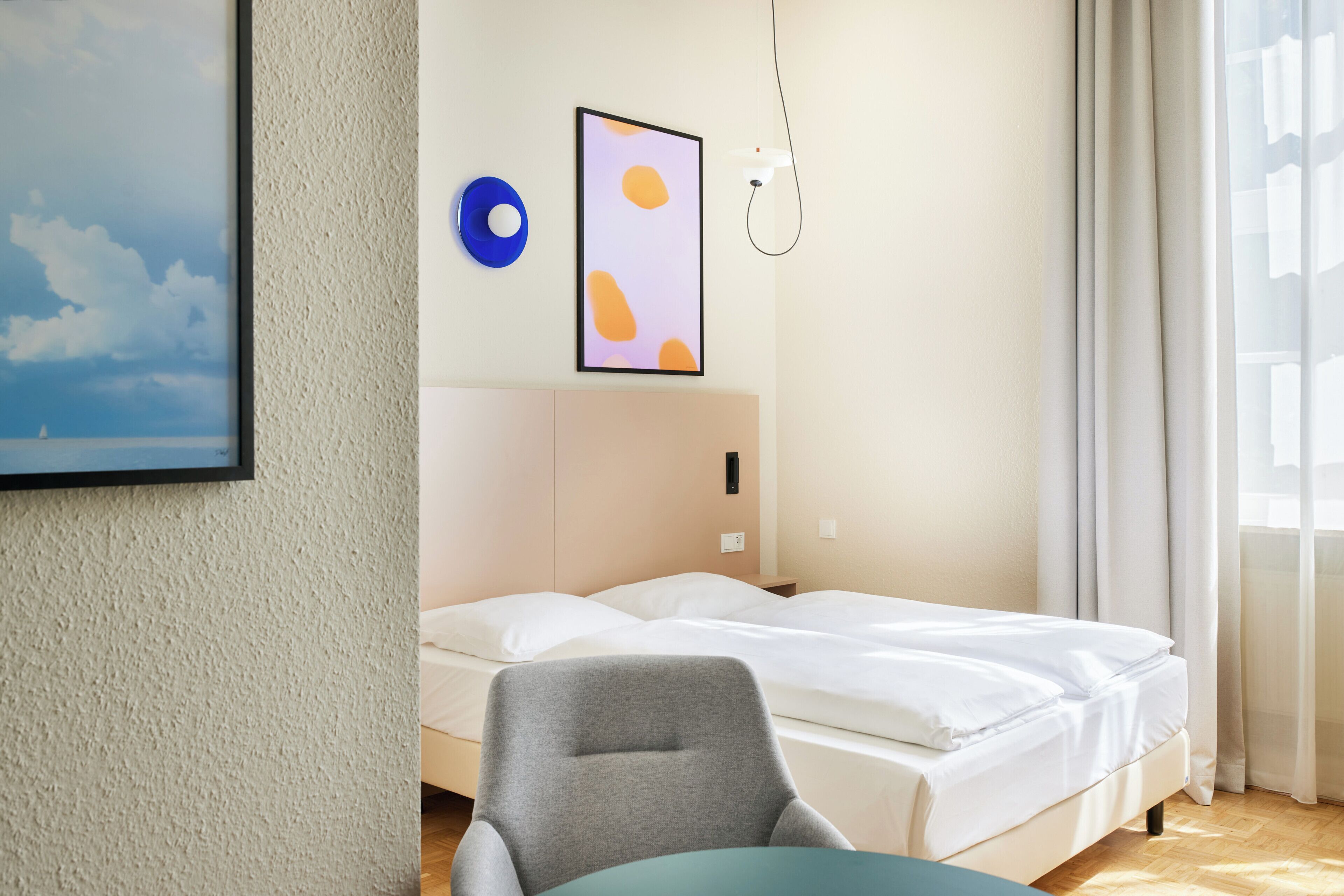 Ett hotellrum med en säng, en stol, ett konstverk som hänger på väggen och ett fönster med gardiner.
