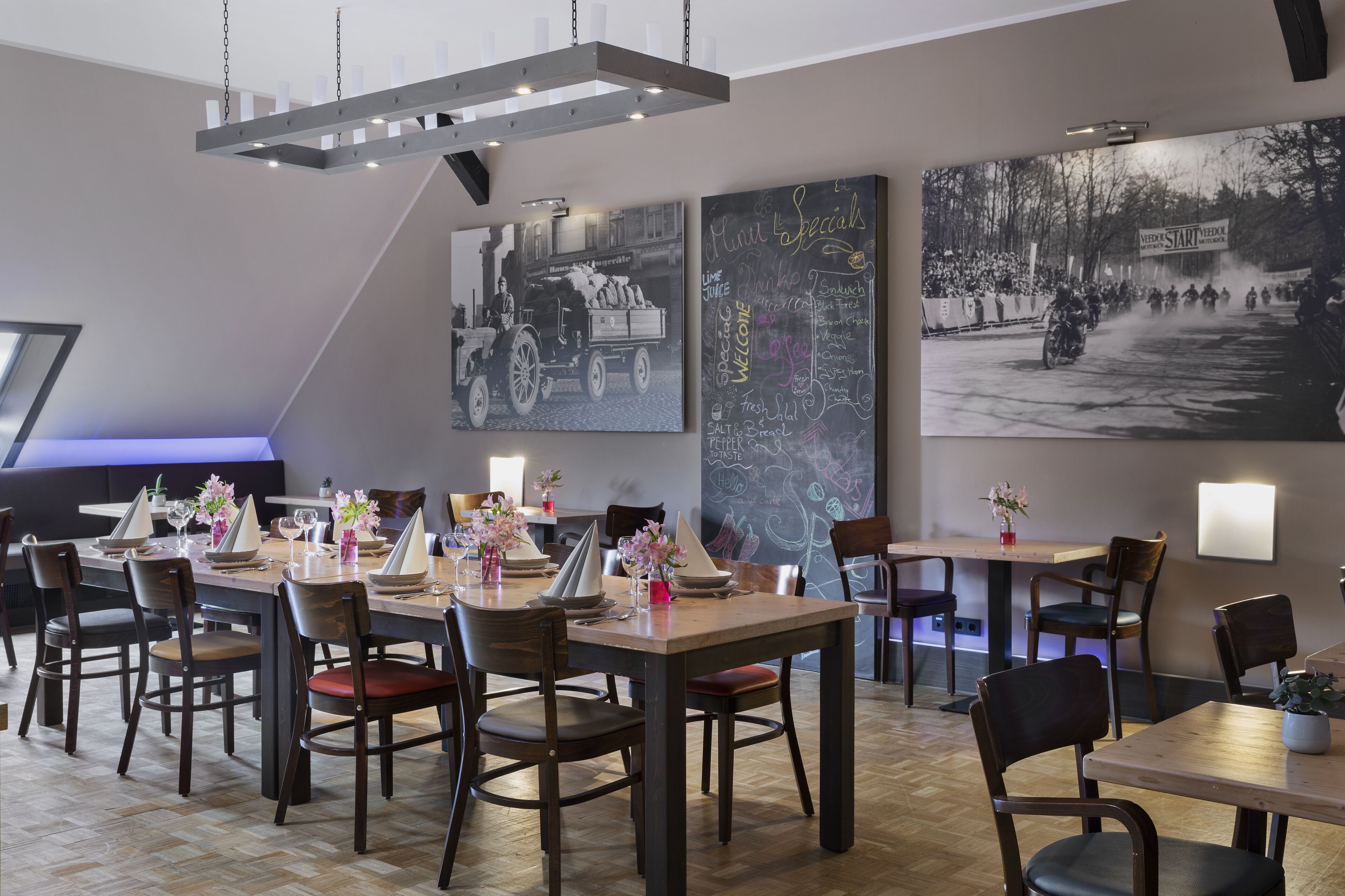 A restaurant with wooden tables and chairs, a chalkboard menu, and vintage photographs on the walls.