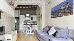 A modern living room with a grey sofa, a flat-screen TV, and a dining area with white chairs and cabinets. - The Ginori  Apartment (Firenze)