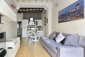 Un salon moderne avec un canapé gris, un téléviseur à écran plat et un coin repas comprenant des chaises et des meubles de rangement blancs.