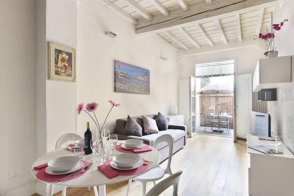 A dining area with a table set for four, a sofa, and a cityscape painting on the wall.