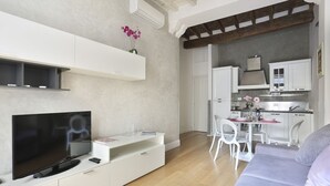 A modern living room with a flat-screen TV, white furniture, a dining area with a table and chairs, and a kitchen with white cabinets. - The Ginori  Apartment (Firenze)