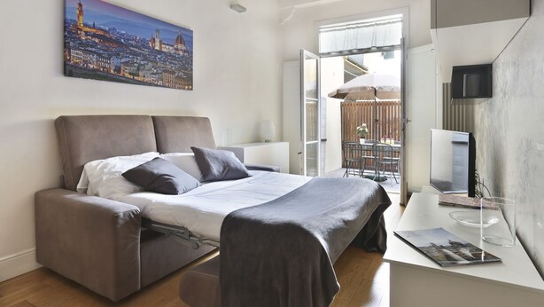 A modern bedroom with a bed, a desk, a TV, and a balcony with a view of a cityscape. - The Ginori  Apartment (Firenze)