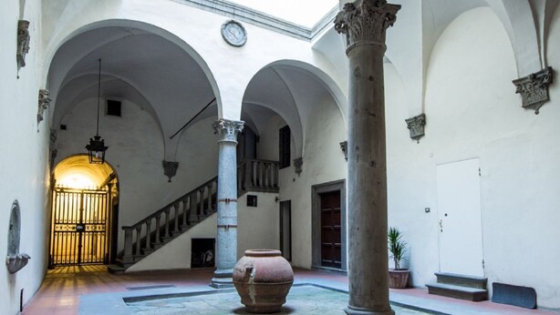 An interior courtyard with arches, a staircase, a large vase, and a potted plant. - Maggio View Apartment (Firenze)