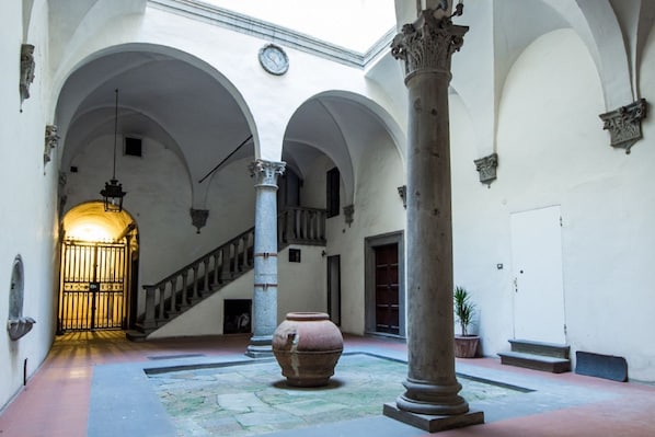 An interior courtyard with arches, a staircase, a large vase, and a potted plant.