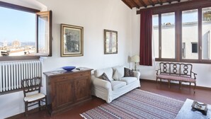 A living room with a sofa, a wooden cabinet, a bench, and a view of a cityscape through large windows. - Maggio View Apartment (Firenze)