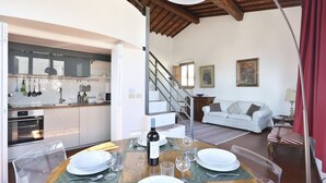 A dining area with a wooden table set for a meal, a kitchen in the background, a staircase, and a living room with a sofa. - Maggio View Apartment (Firenze)