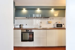 A modern kitchen with white cabinets, a stainless steel oven, a microwave, and a coffee maker.