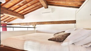 A bedroom with a wooden ceiling, a bed with white and brown bedding, and a window with a red curtain. - Maggio View Apartment (Firenze)