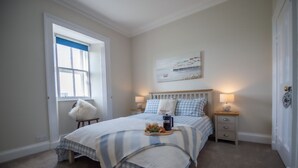 Une chambre à coucher avec un lit, des tables de chevet, une fenêtre et un tableau au mur.