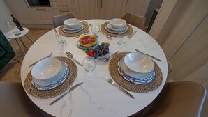 Une table de salle à manger ronde, mise avec des assiettes, des bols et des couverts, entourée de chaises.