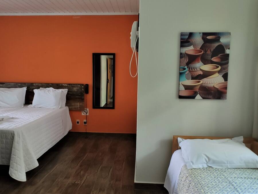 A hotel room with two beds, an orange wall, a wooden headboard, a painting of pottery, and a window with curtains.
