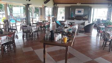 A restaurant with wooden tables and chairs, a tiled floor, and a view of the outdoors.