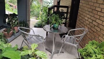 A small patio area with a round metal table and two metal chairs, surrounded by potted plants and a brick wall.