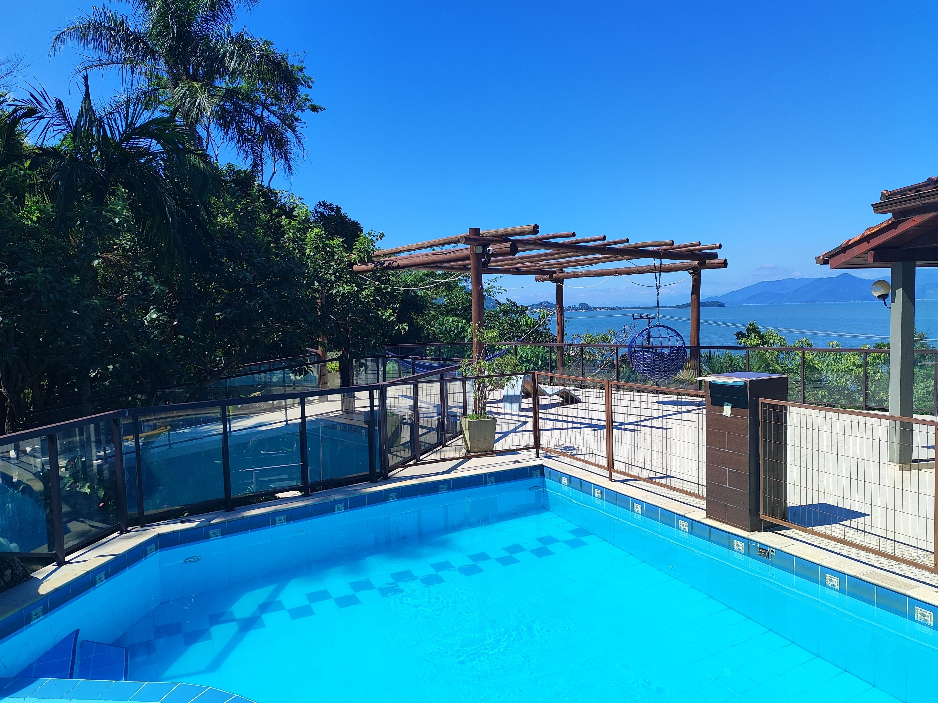 Zwembad met een pergola, glazen balustrade en uitzicht op zee en bergen.