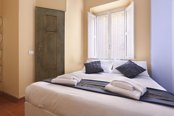A neatly made bed with pillows, a window with blinds, and a door.