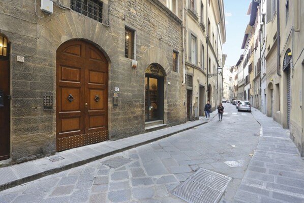 A stone building with a large wooden door, a small shop entrance, and a narrow street.