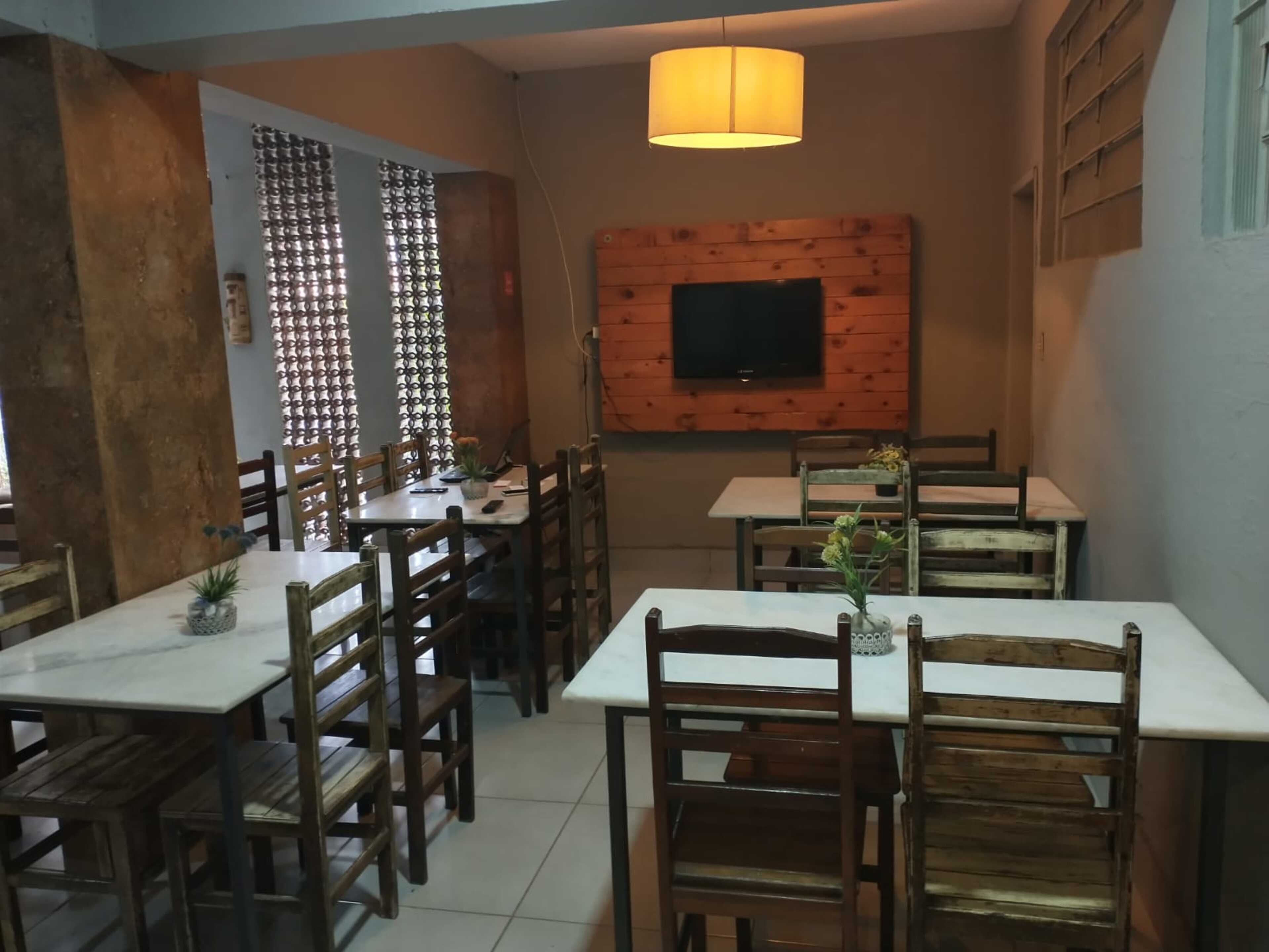 Um restaurante com mesas e cadeiras de madeira, uma TV presa a uma parede de madeira e um lustre pendurado.