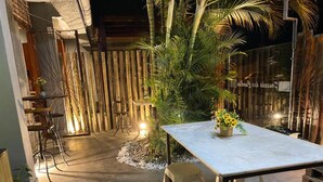 Un patio al aire libre con una mesa y taburetes, rodeado por una cerca de madera y plantas tropicales.