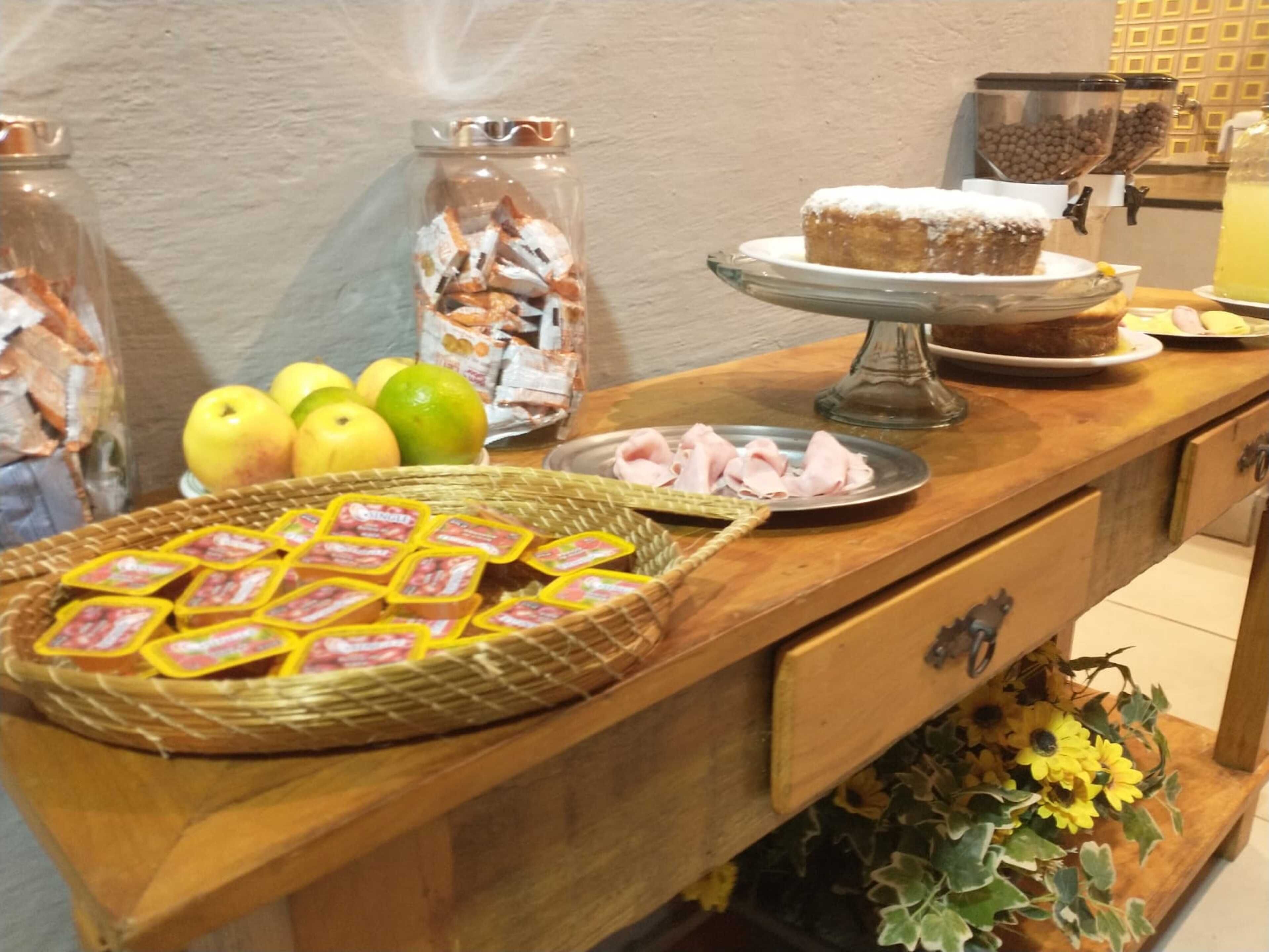 A buffet table with various food items, including a cake on a stand, a plate of sliced meat, and a basket of wrapped pastries.
