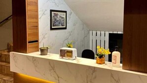 Un mostrador de recepción con encimera de mármol y detalles de madera, un cuadro en la pared y una pequeña planta en maceta.
