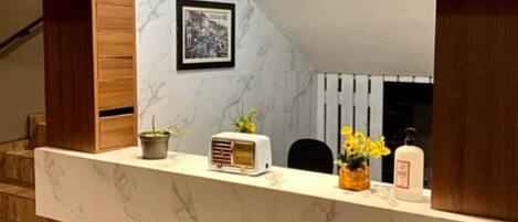 A reception desk with a marble top and wooden accents, a framed picture on the wall, and a small potted plant.