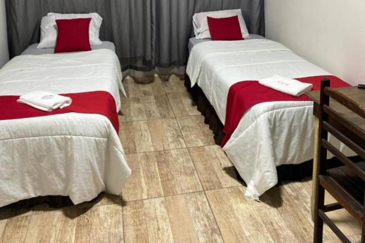 Una habitación con dos camas, cortinas grises y una silla de madera.
