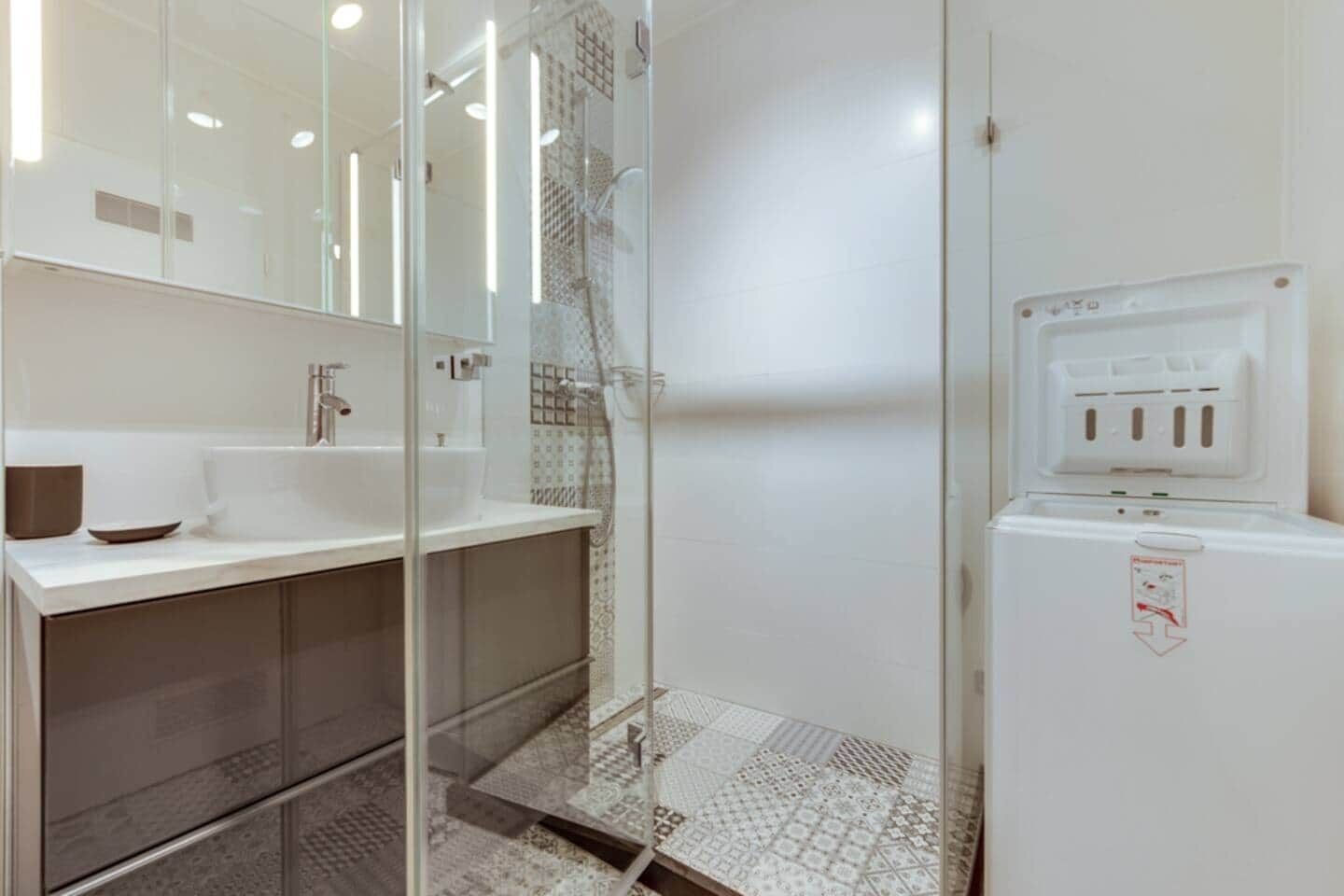 A modern bathroom with a glass shower enclosure, a white sink, and a built-in heater.