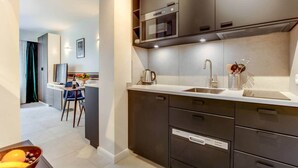 A modern kitchen with dark cabinetry, a stainless steel sink, and a microwave. There is a dining area with a table and chairs visible in the background. - Studio Sarah 4* super central near Sofitel (Luxembourg)