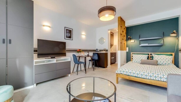 A modern bedroom with a bed, a TV, a desk, and a glass coffee table. - Studio Sarah 4* super central near Sofitel (Luxembourg)