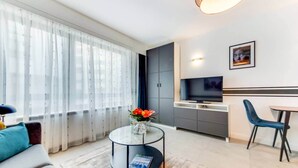A modern living room with a sofa, a coffee table with a magazine, and a kitchen area with a TV and cabinets. - Studio Sarah 4* super central near Sofitel (Luxembourg)