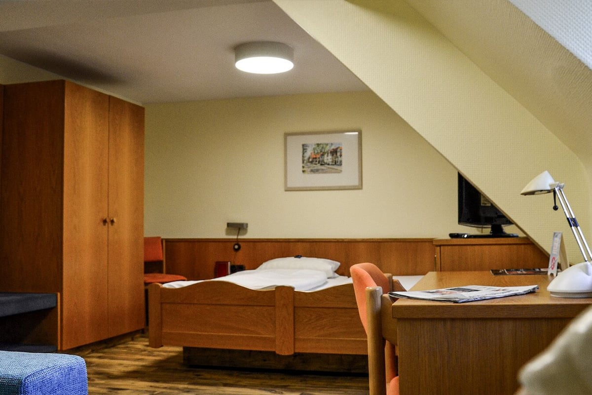 A hotel room with a bed, a desk with a lamp, a television, and a framed picture on the wall.