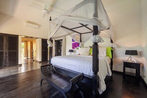 A bedroom with a four-poster bed, a bench, a nightstand, and a ceiling fan.
