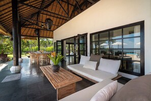 A modern outdoor seating area with a wooden table, a sofa, and a large window overlooking a pool.