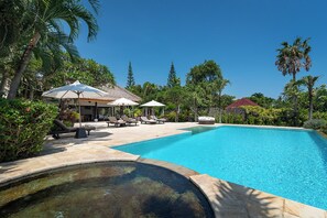 A swimming pool with lounge chairs and umbrellas, surrounded by palm trees and a clear sky.