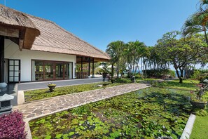 A building with a thatched roof, a stone pathway, and a pond with lily pads.