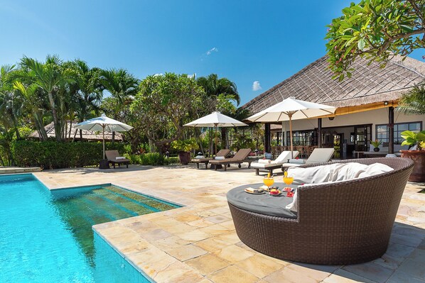 A poolside area with lounge chairs, umbrellas, and a wicker sofa.