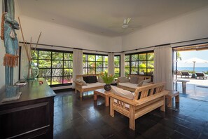 A spacious room with large windows, a ceiling fan, and a view of the ocean.