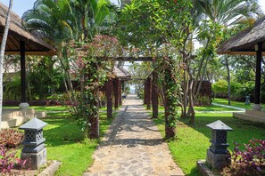 A stone pathway leading through a garden with a thatched-roof structure and stone lanterns.