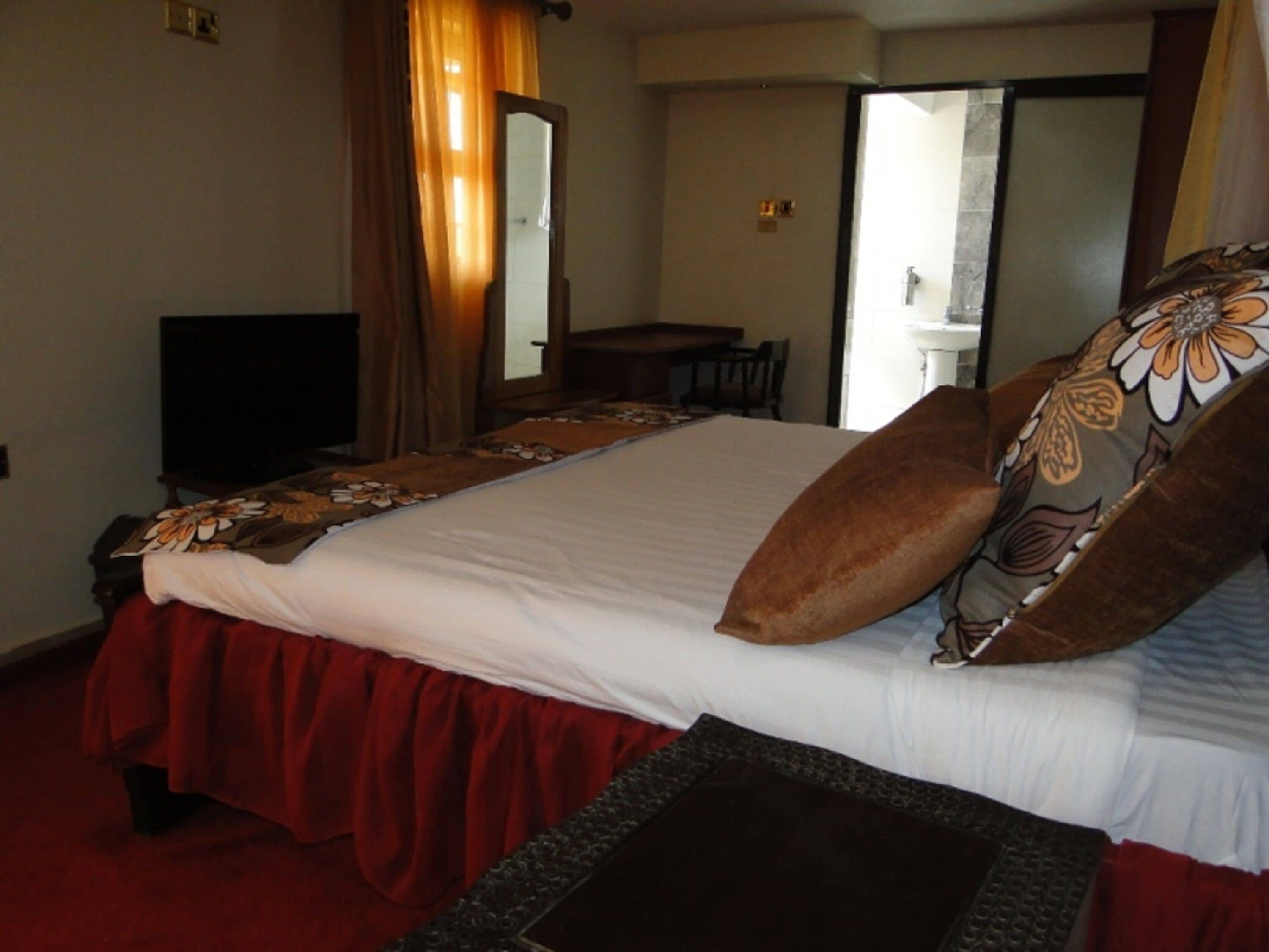 Habitación de hotel con una cama grande, televisión, escritorio y baño visible a través de una puerta abierta.