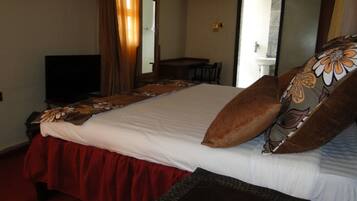 Habitación de hotel con una cama grande, televisión, escritorio y baño visible a través de una puerta abierta.